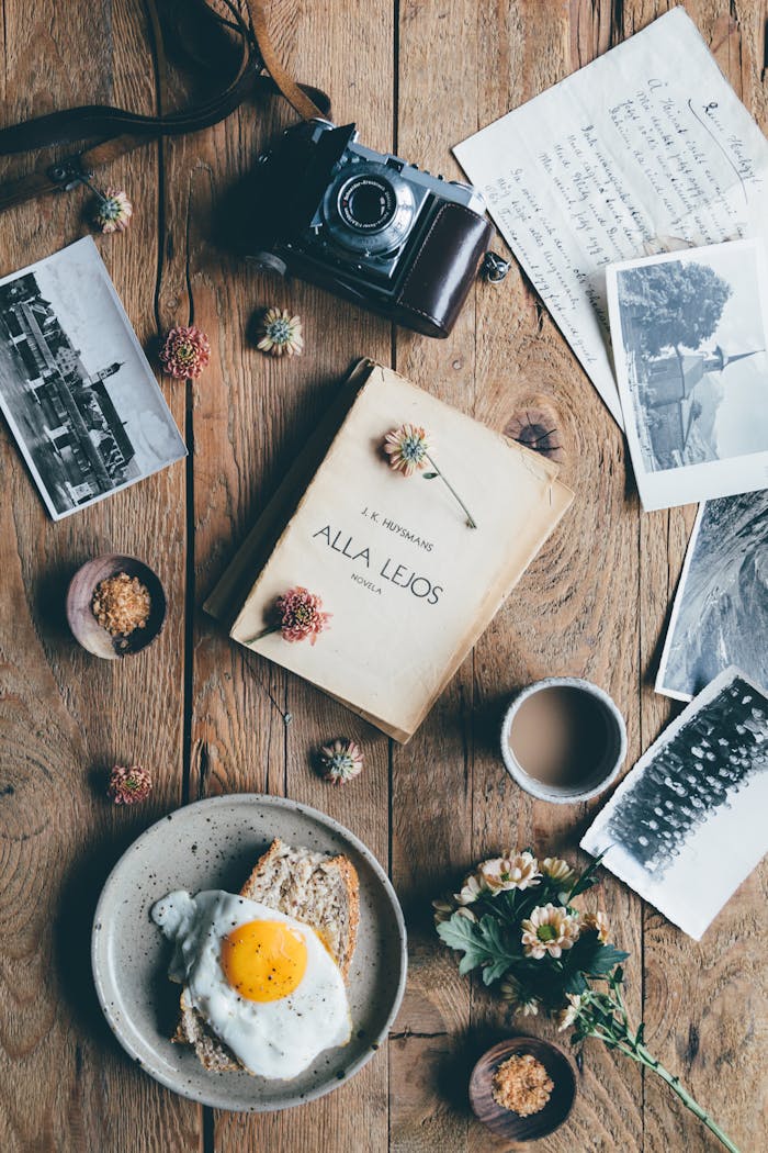 Top view of fresh coffee and tasty meal near retro camera and old pictures on wooden table
